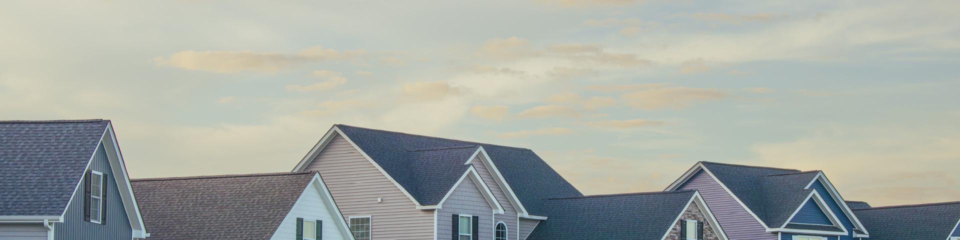 The tops of a row of houses set against a beautiful pastel sky at sunset.