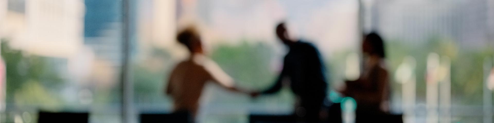 Blurred silhouette of business partners shaking hands in a boardroom setting