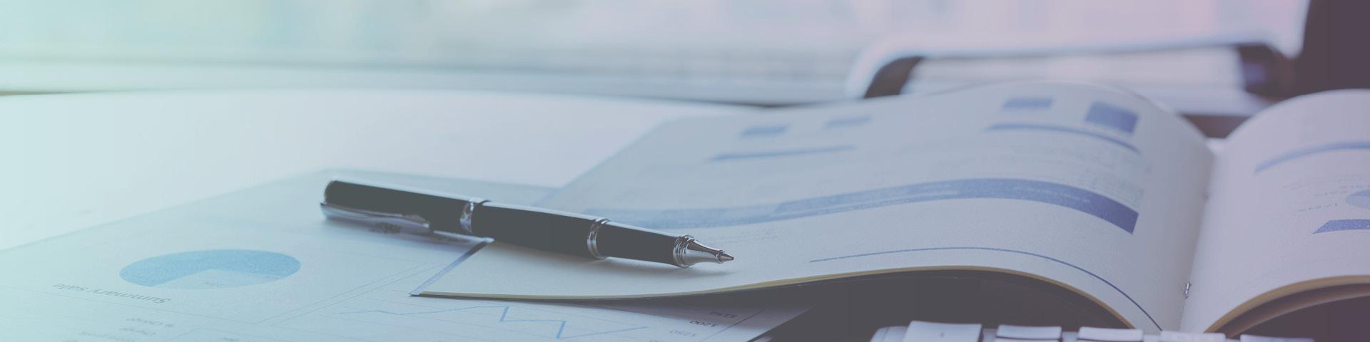 Pen next to reports opens on desk featuring charts and graphs.