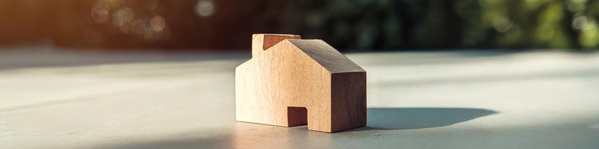 Small wooden toy house shape sitting on a concrete pad, greenery in the background.